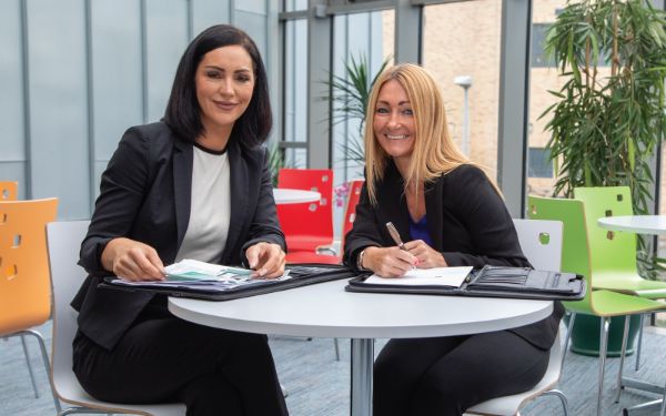 2 females sitting at a table and smiling for the camera. 